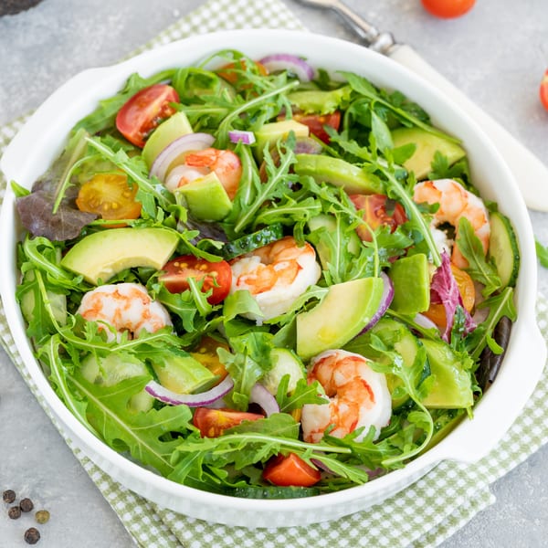 Fresh shrimp and avocado salad with arugula, cherry tomatoes, and red onion in a white bowl.