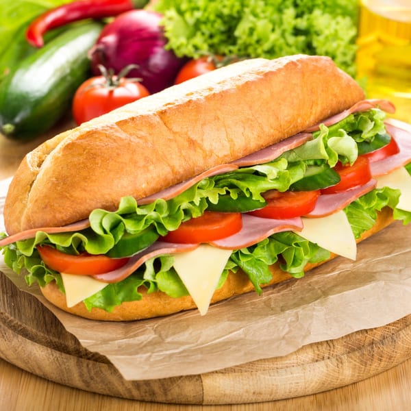 A large, fresh submarine sandwich with ham, cheese, lettuce, and tomatoes on a wooden board.