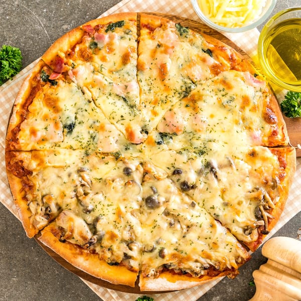 Oven King Pizza's sliced pizza with melted cheese, ham, and mushrooms on a wooden board.
